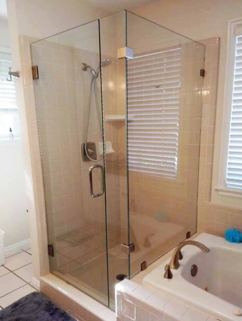 Bathroom with warm colors, golden accessories, and frameless shower enclosure.
