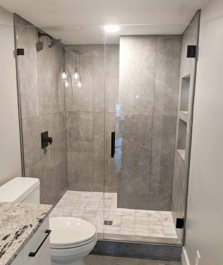 Non rectangular shower in a bathroom divided by a frameless glass wall.